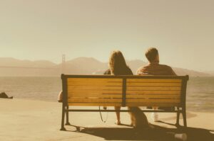 psychothérapie pour couple - un homme et une femme sont assis côte à côte sur un banc, face à un paysage flou. On les voit de dos.