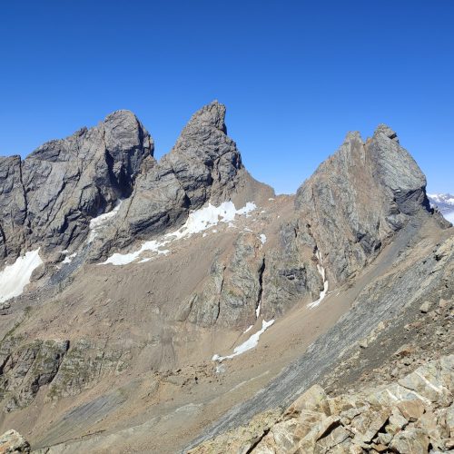 3 sommets de montagnes sur fond de ciel bleu. Au pied des sommets, des pierres, rien que des pierres, des champs de pierres.
